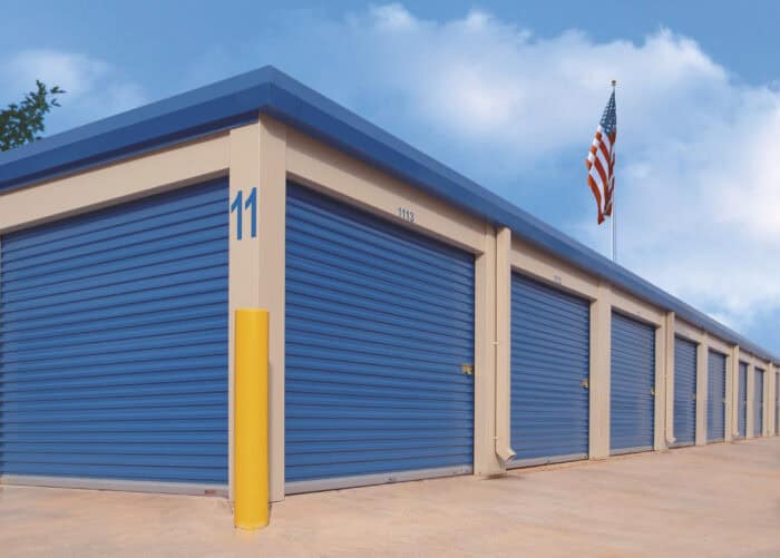 Row of blue storage units with closed doors, labeled number 11 on one unit, under a blue sky. An American flag is mounted on the building.