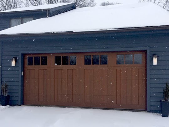 Wood garage door on a blue home that is covered in snow